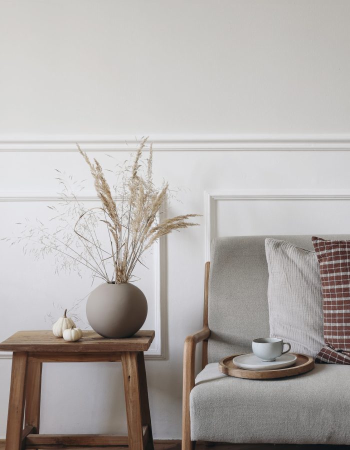 Dry grass bouquet in ball shaped vase. Midcentury sofa with cup of coffee, checkered linen cushions, blanket. Little white pumpkins, old side table. Autumn interior, Thanksgiving, Halloween.